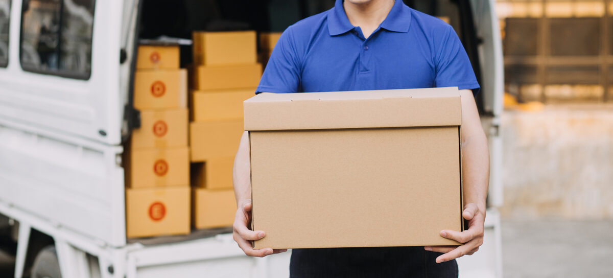 Parcel delivery. Delivery man outside holding package. Truck behind him.