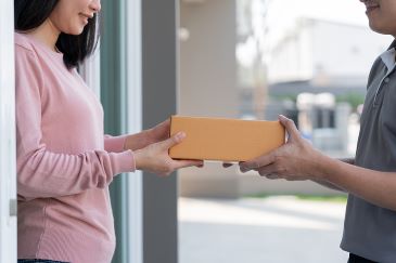 Happy, smiling woman receives parcel from courier in front house.