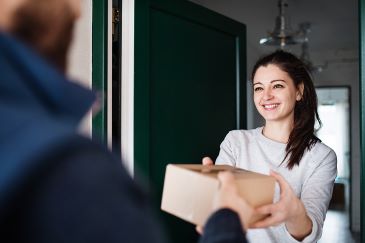 Woman receiving parcel from unrecognizable delivery person at the door 