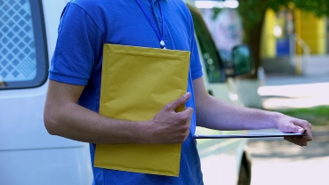 Courier holding yellow package and proof delivery form, documents shipping
