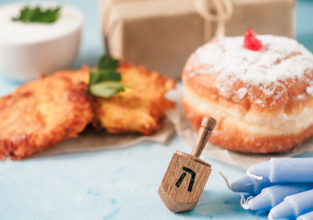 Jewish holiday Hanukkah concept and background. Hanukkah food doughnuts and potatoes pancakes latkes, giftbox, candle and traditional spinnig dreidl on blue background. Copy space for text.